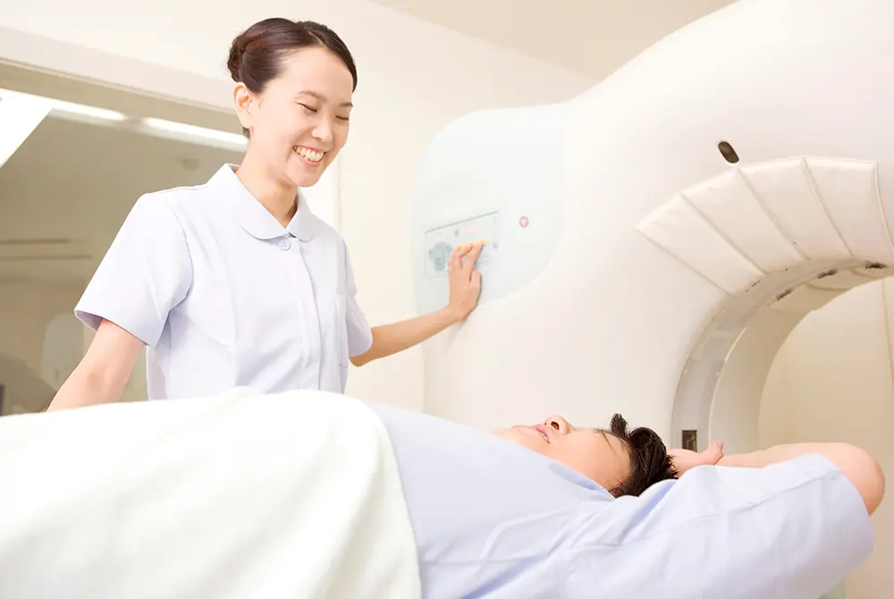 CT検査装置の操作を行う医療従事者と、検査台に横たわる患者。