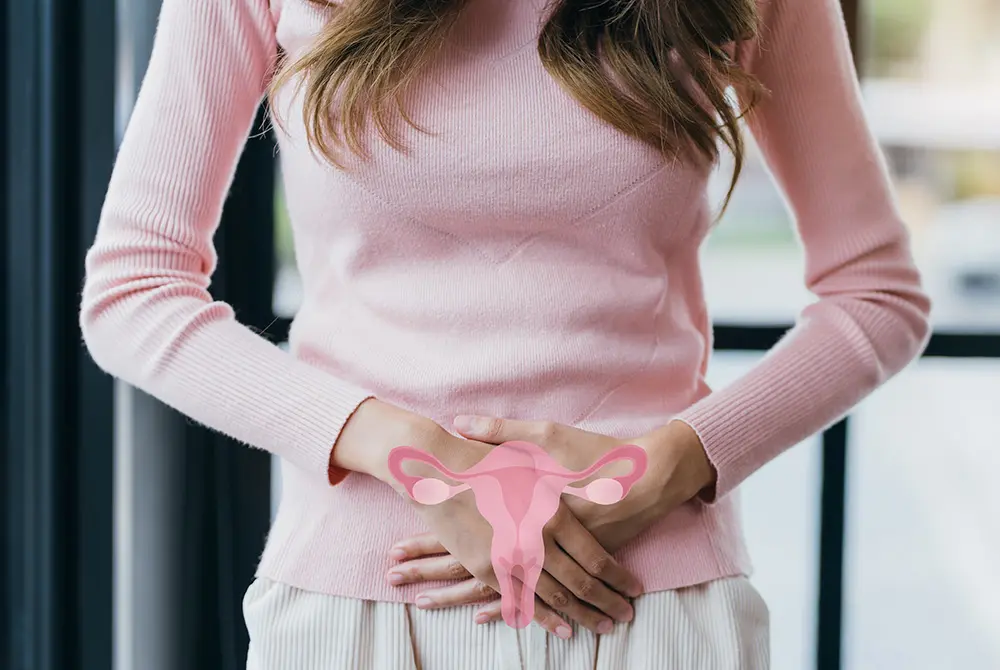 下腹部に手を当て、子宮のイラストが重ねて表示された女性の様子。