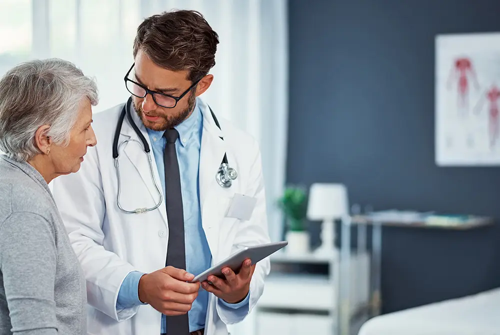医師が高齢の女性患者にタブレットを見せながら説明している様子。
