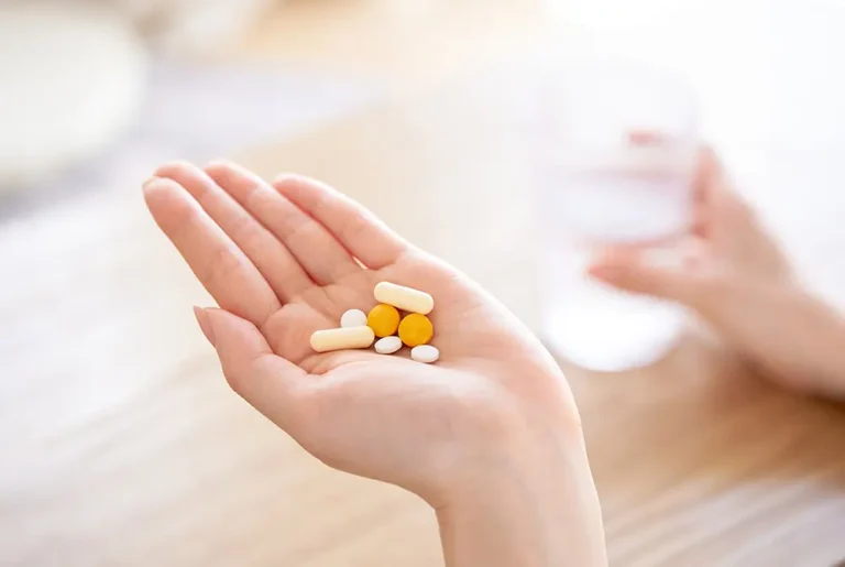 手のひらに複数の錠剤やカプセルを載せ、水を手にして服用しようとしている様子。
