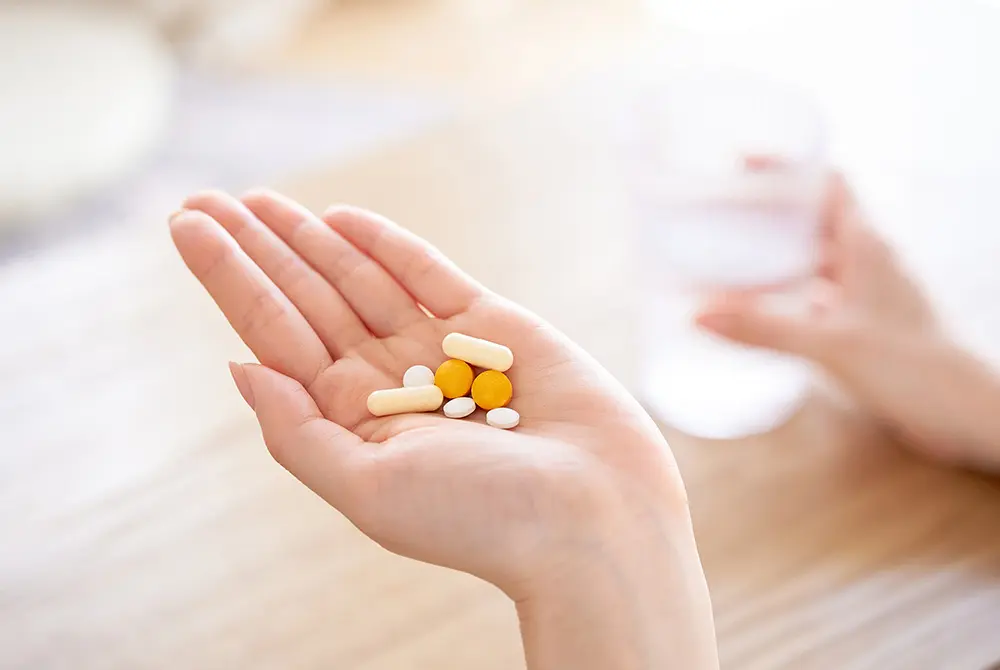 手のひらに複数の錠剤やカプセルを載せ、水を手にして服用しようとしている様子。