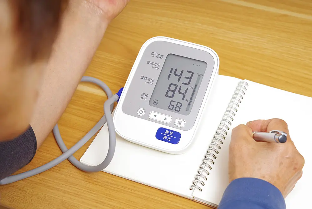 家庭用血圧計で測定した数値をノートに記録している様子。