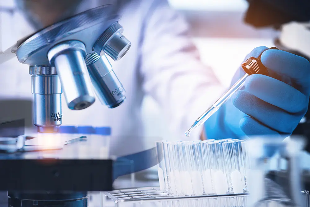 顕微鏡と試験管を用いて実験を行う研究者の手元。