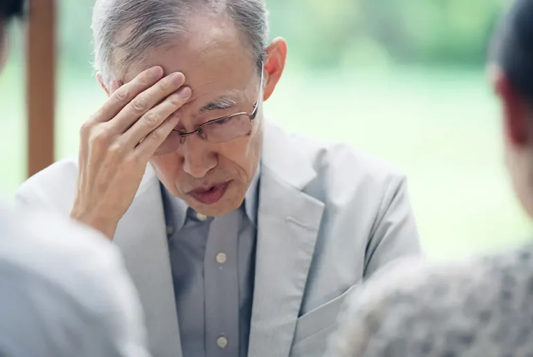 額に手を当て、悩んだ様子を見せる高齢男性。