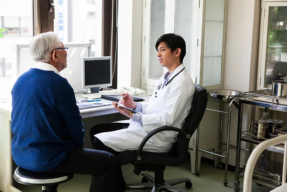 医師が高齢男性に説明をしている診察室の様子。