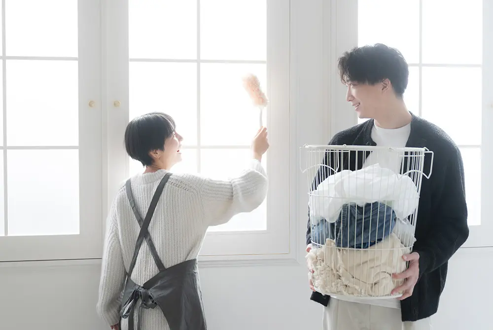 洗濯かごを持つ男性と、はたきを持つ女性が向かい合っている様子。
