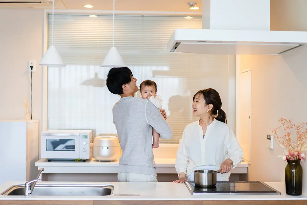 キッチンで父親が赤ちゃんを抱き、母親が調理している様子。