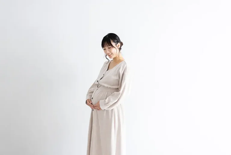 お腹に手を添えて微笑む妊婦