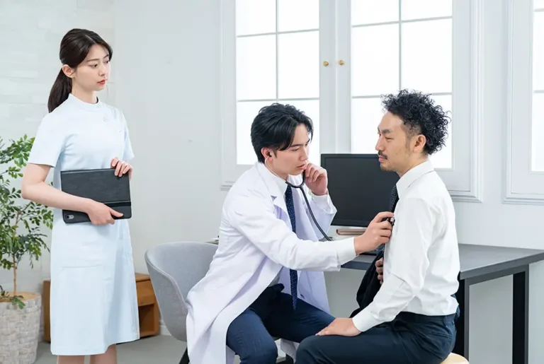 医師が聴診器で男性患者の胸部を診察している様子