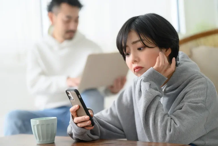 スマートフォンを見ながら悩んだ表情を浮かべる女性