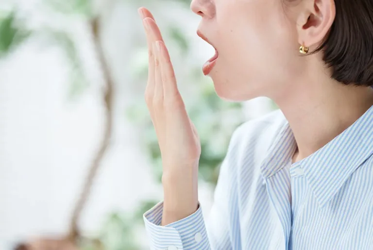 手で口元を覆い息のにおいを確認する女性