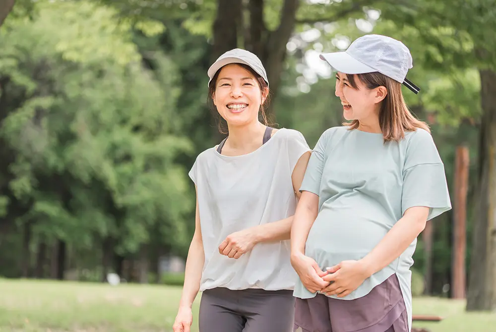 屋外で会話しながら歩く妊婦と女性