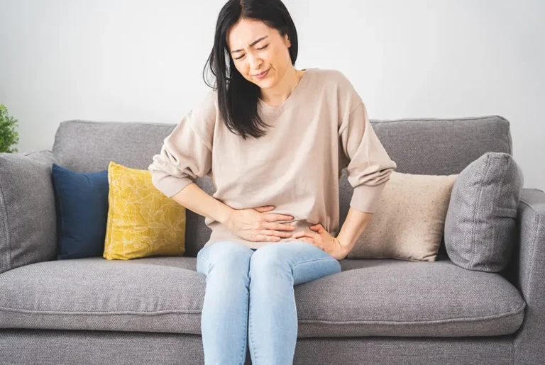 ソファに座り腹部の痛みで顔をしかめる女性