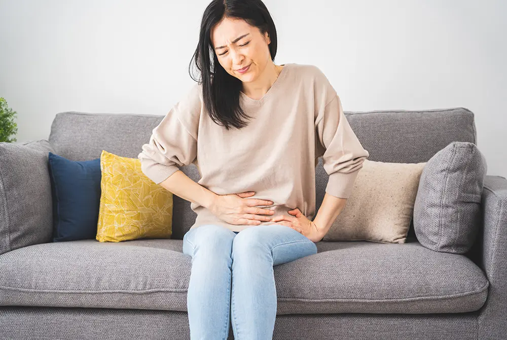 ソファに座り腹部の痛みで顔をしかめる女性