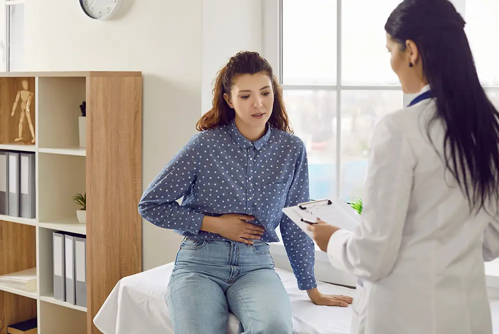 腹部を押さえながら医師の診察を受ける女性