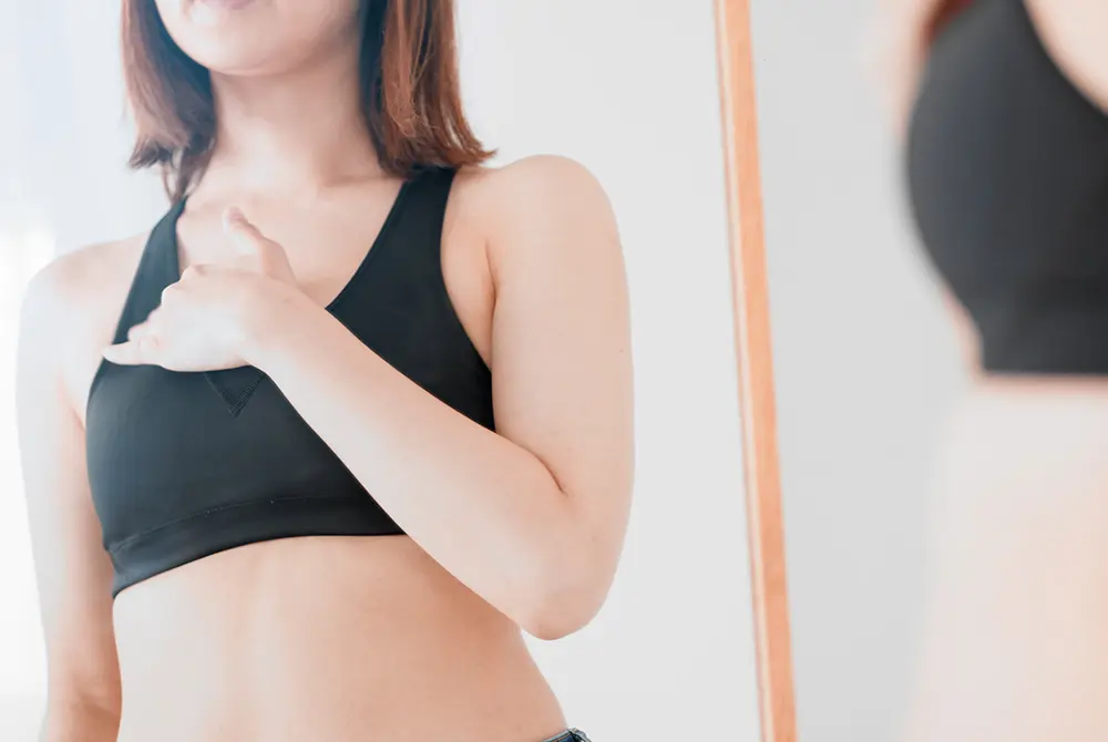 鏡の前で胸元に手を当て、乳房の状態を確認している女性。