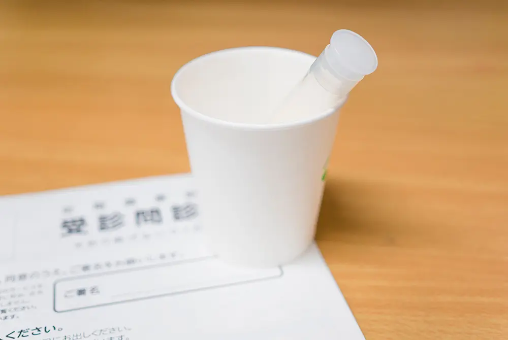 採尿カップと検査用の容器が問診票の上に置かれている様子
