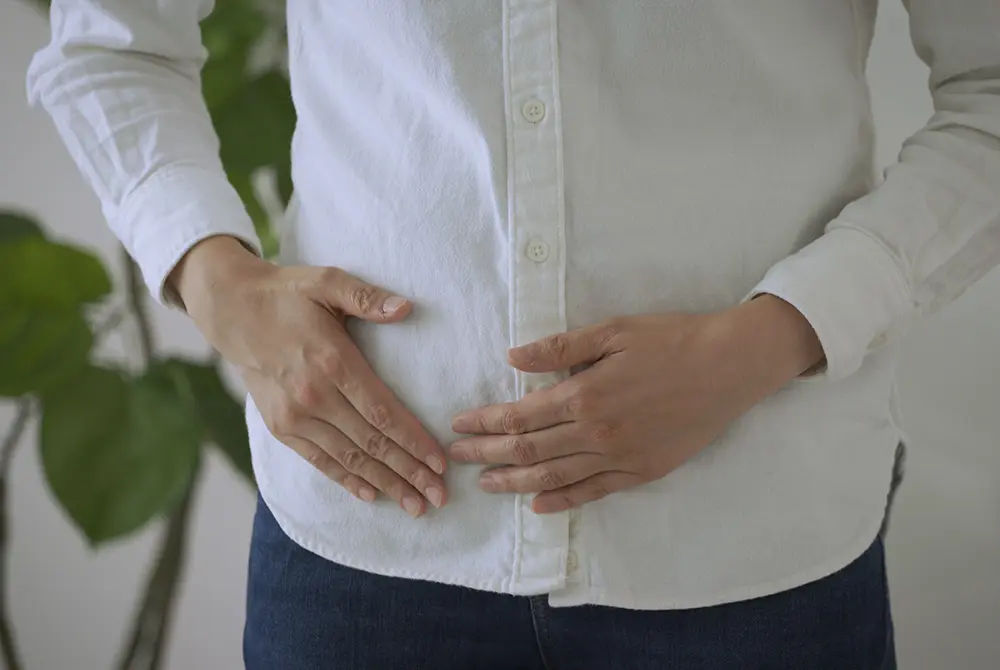 下腹部に手を当てて不調を感じている男性の様子