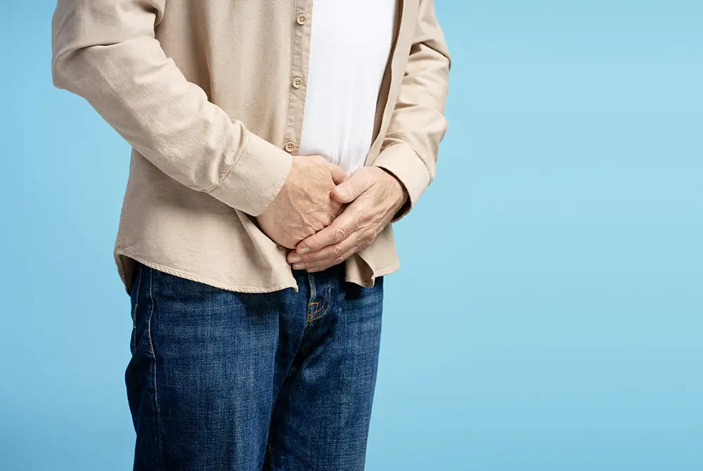 下腹部に両手を当てる男性の上半身。排尿トラブルや下腹部の不調を示すイメージ。
