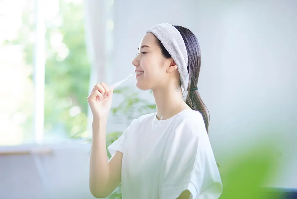 洗面後の女性が歯ブラシを口元に当て、歯みがきをしている様子。