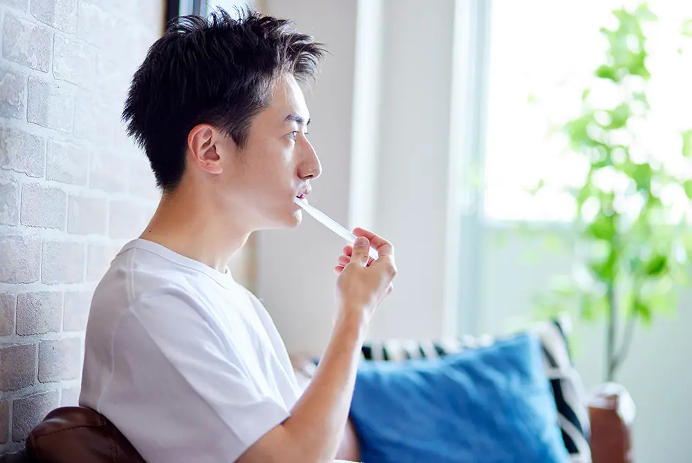 室内で歯ブラシを口元に当てる男性。歯みがきによる口腔ケアを示すイメージ。