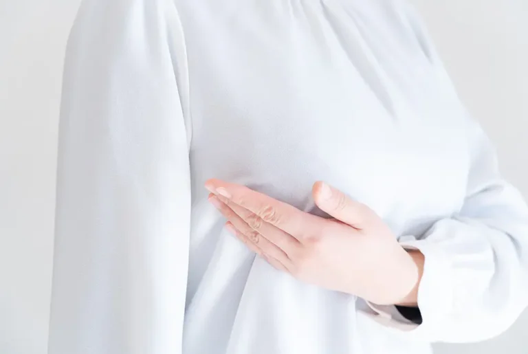 胸に手を当てる女性の上半身。乳房の違和感やセルフチェックを示すイメージ。