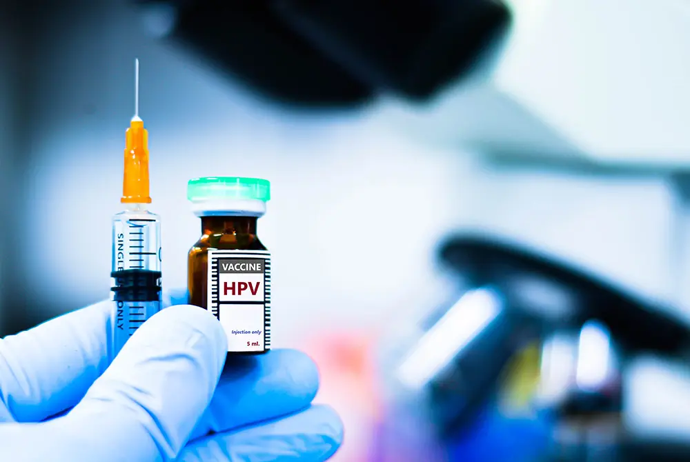HPVワクチンと書かれたバイアルと注射器を、手袋を着けた手が持っている様子。