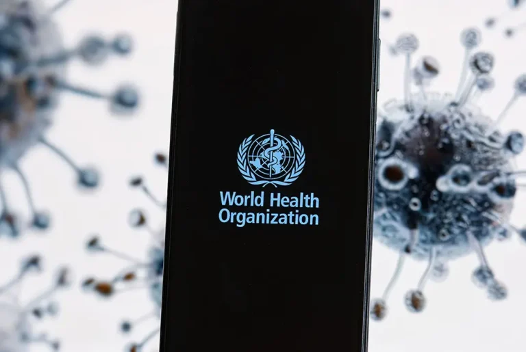 世界保健機関（WHO）のロゴが表示されたスマートフォンと、背景にあるウイルスのイメージ。