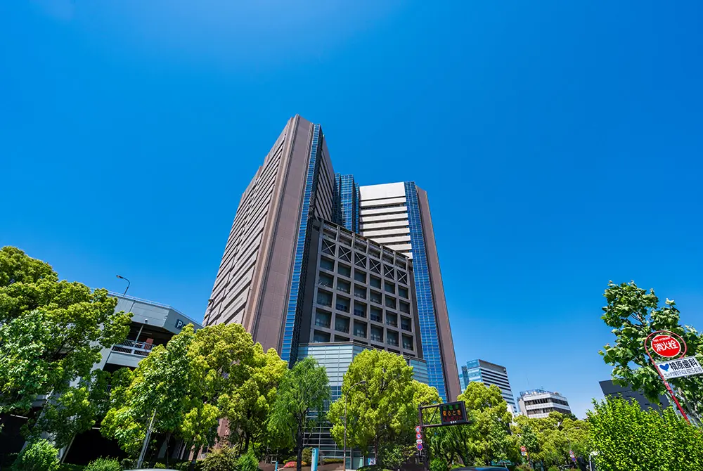 青空の下、緑の木々に囲まれた都市部の高層ビル。