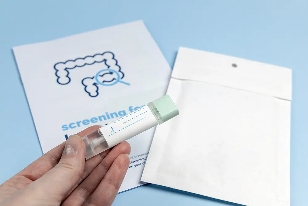 大腸の図が描かれた検査キットの前で、採便用の容器を手に持つ様子。
