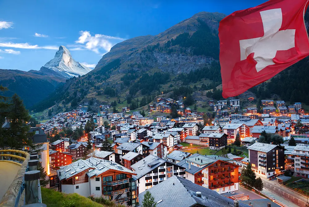 スイス国旗が掲げられた山あいの街並みと、背景にそびえるマッターホルン。