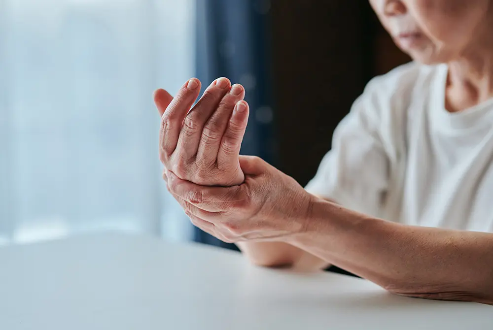手首を押さえる高齢女性。関節の痛みやこわばりを示す様子。