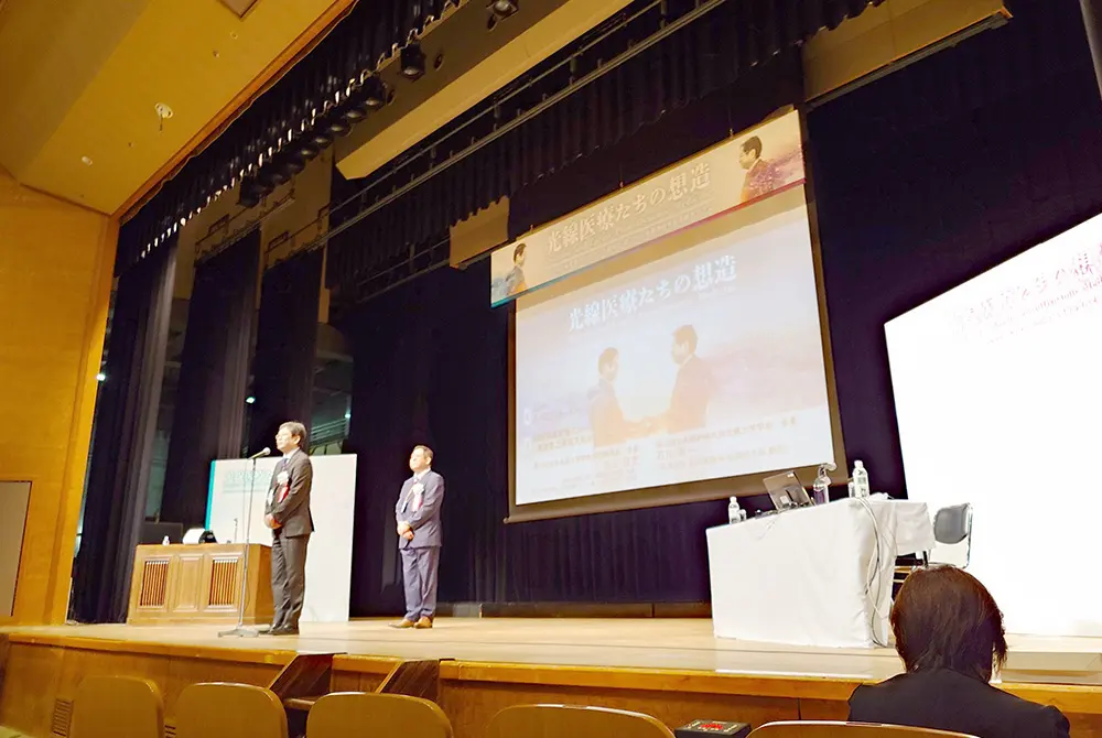 第36回日本光線力学学会学術講演会と第22回日本脳神経外科光線力学学会の会長2人が、会場ステージで挨拶している様子。