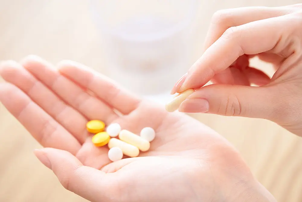 手のひらにのせた錠剤やカプセルを、もう一方の手で取ろうとしている様子。