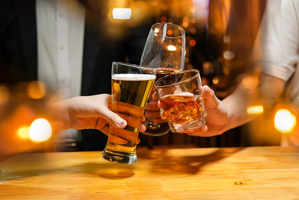バーのような場所で、ビールや酒の入ったグラスを持ち寄って乾杯している様子。