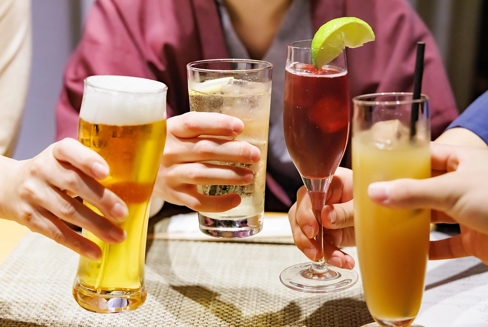 ビールやカクテルなどのグラスを手に持ち、乾杯しようとしている様子。