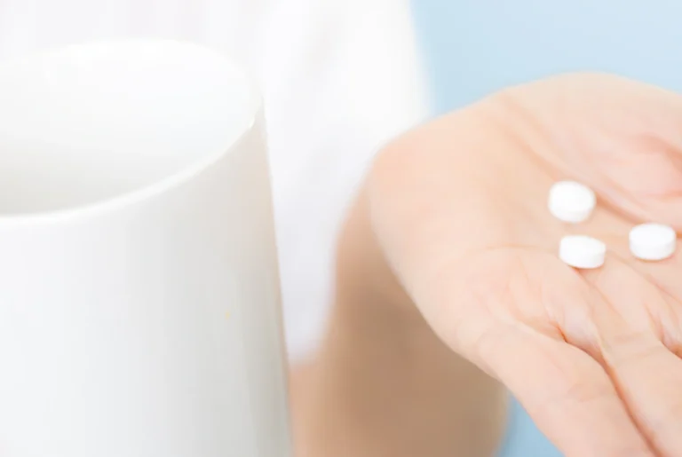 手のひらに白い錠剤をのせ、そばにコップが置かれている様子。