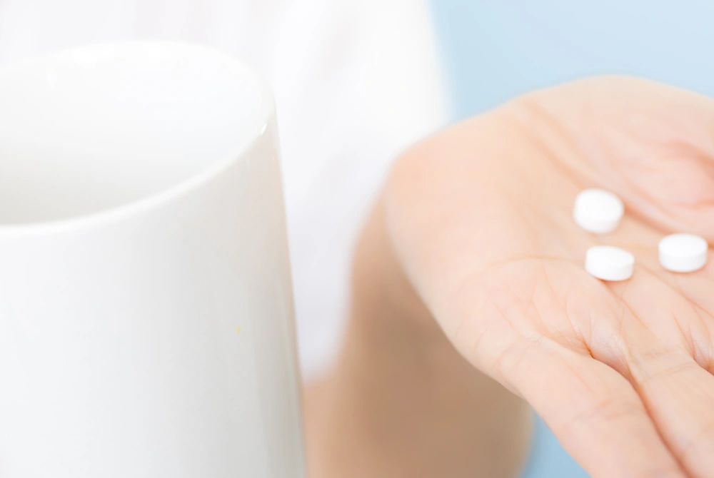 手のひらに白い錠剤をのせ、そばにコップが置かれている様子。