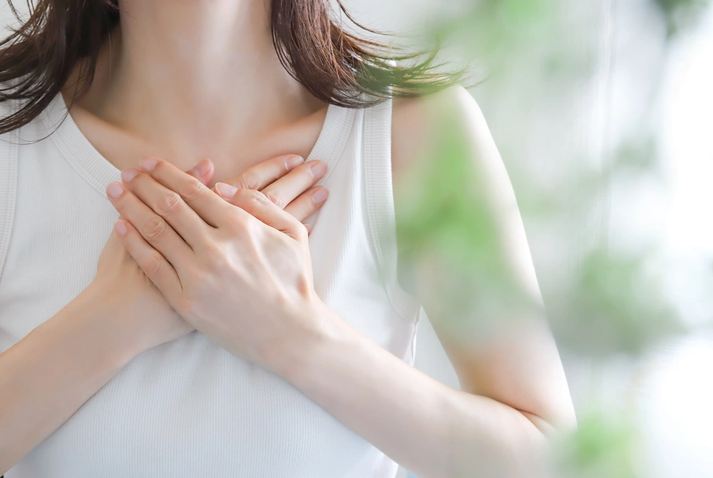 胸元に両手を当てる女性の上半身。