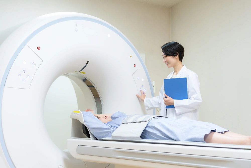 CT検査装置の検査台に横たわる患者に、医療スタッフが声をかけている様子。