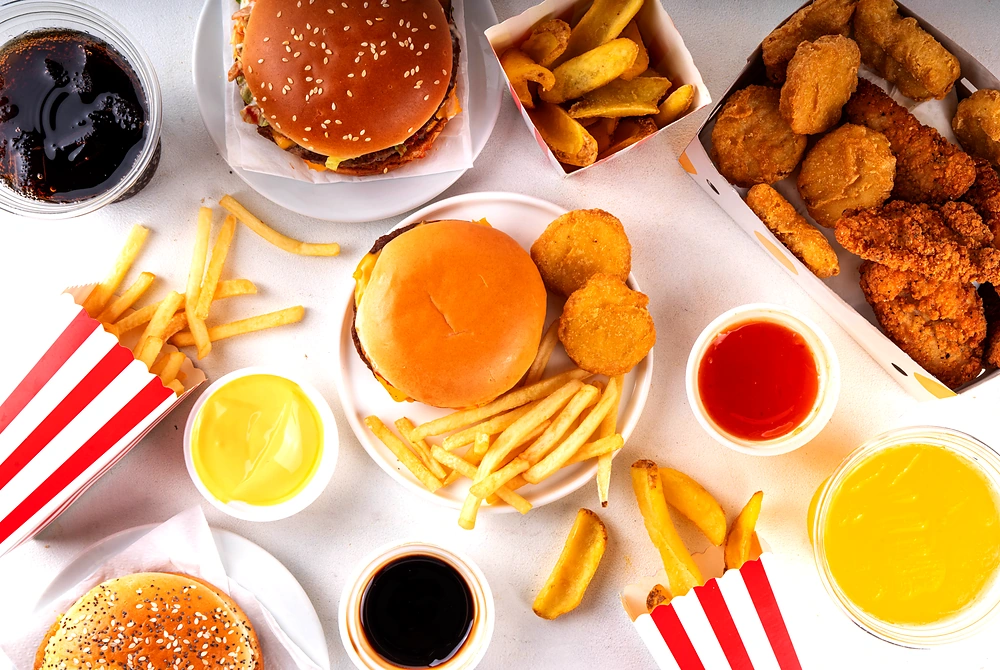 ハンバーガーやフライドポテト、揚げ物、飲み物がテーブルに並んでいる様子。