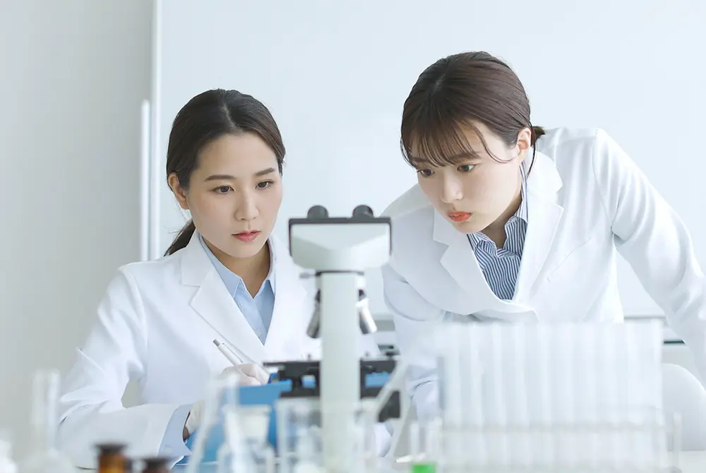 白衣を着た2人の研究者が、顕微鏡を使って観察している様子。