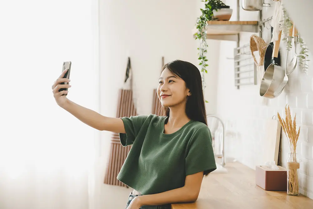 室内でスマートフォンを使い、自分を撮影する女性。