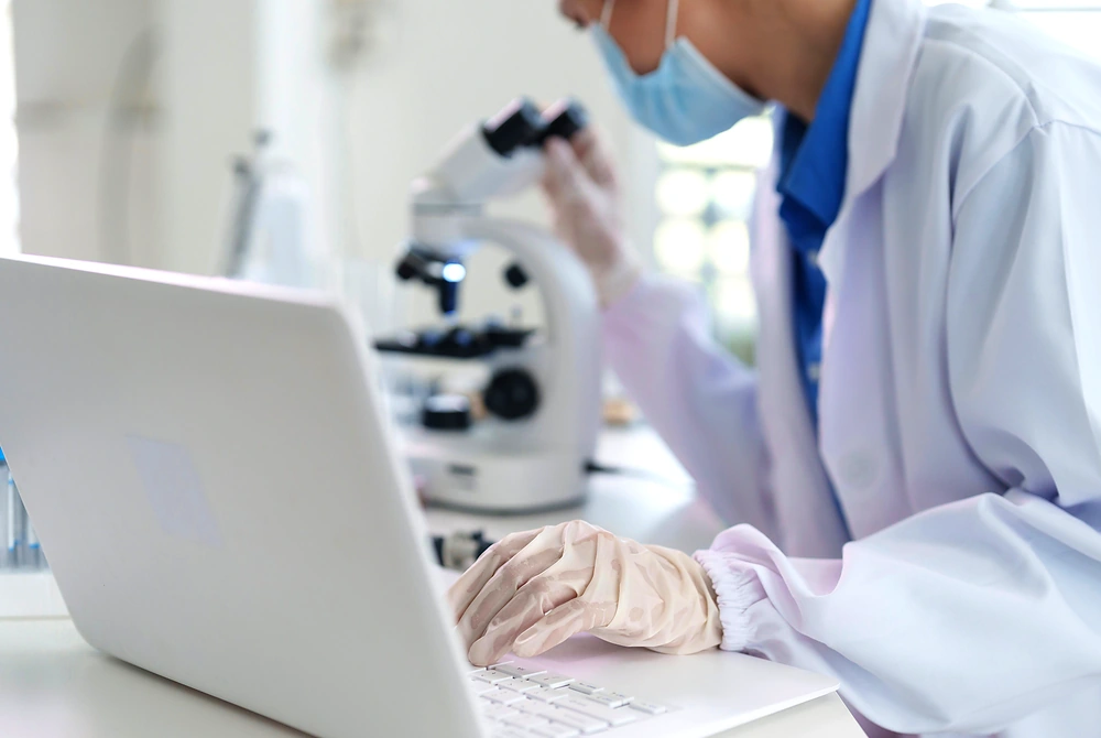 研究者が顕微鏡をのぞきながら、ノートパソコンでデータを確認している様子。