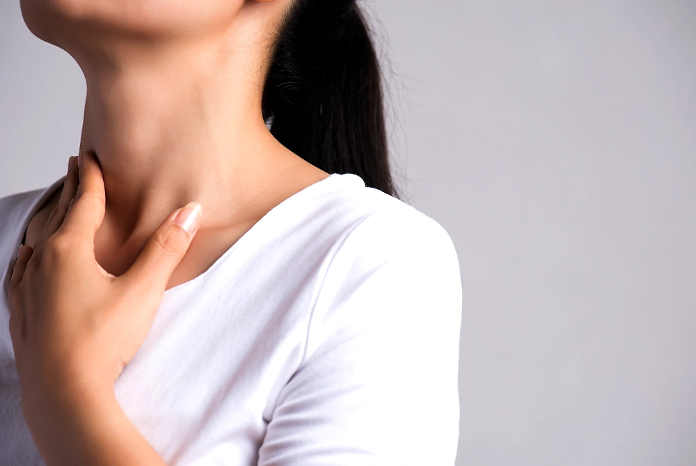 女性が首元に手を当て、甲状腺のある部位を気にしている様子。