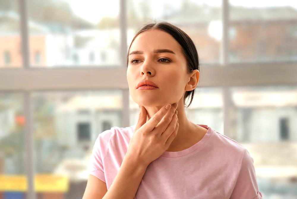 女性が首の前側に手を当て、甲状腺周辺を示している様子。