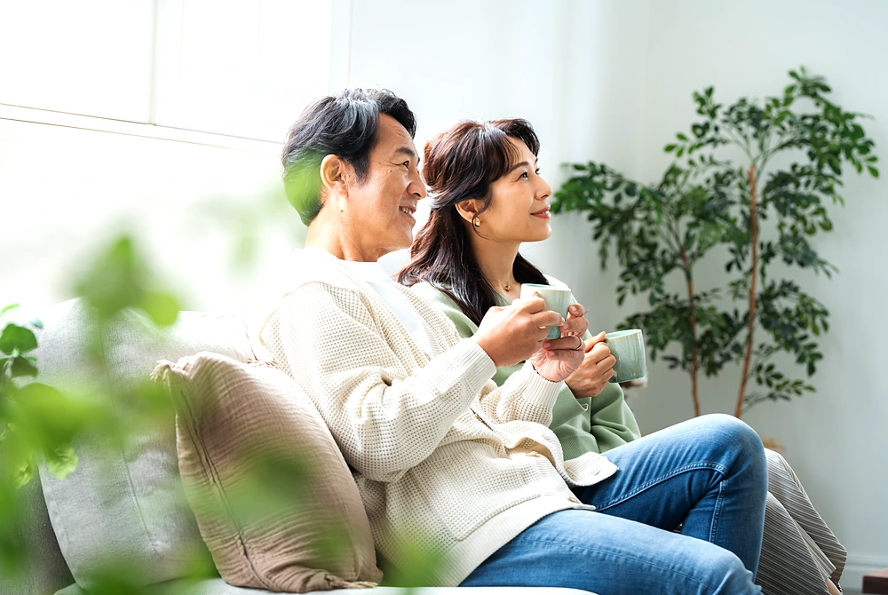 明るい室内でカップを持ちながら並んで座る中年の男女。