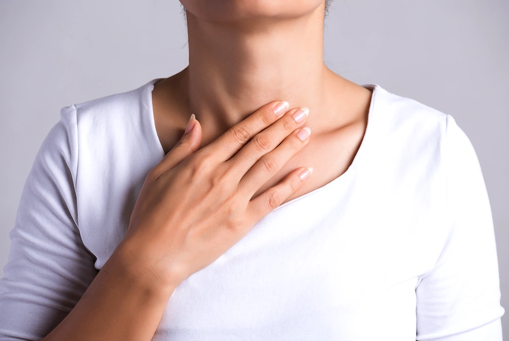 のどの前側に手を当てて、首まわりの違和感を確かめる女性。