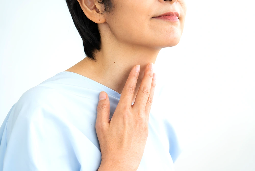 首の前側に指を当てて、甲状腺周辺を確認する医療従事者風の人物。