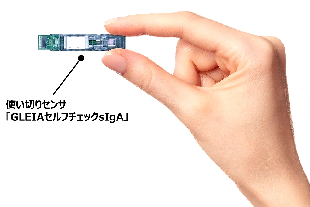 指でつままれた使い切りセンサー「GLEIAセルフチェックsIgA」。